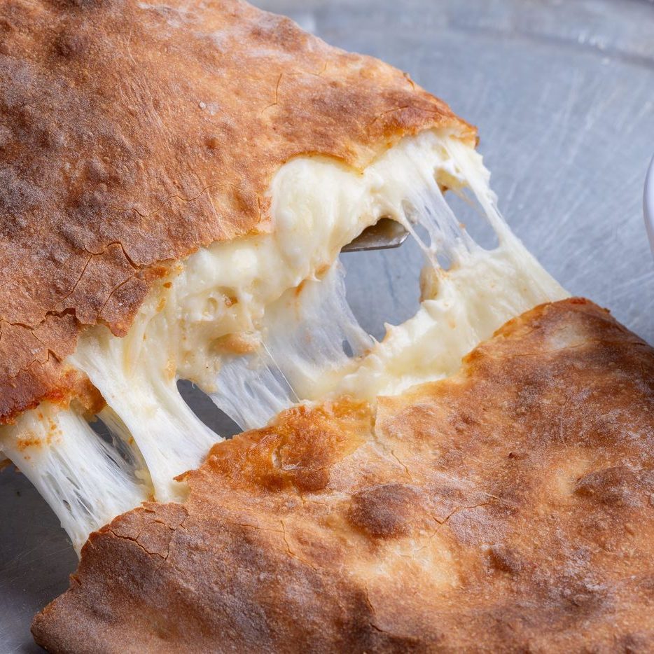 A calzone pulled open with the cheese stretching, cropped square