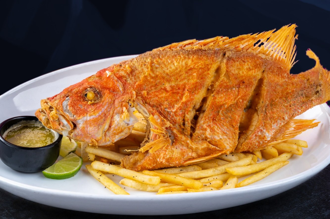 A whole fried red snapper with fries, lime and a green sauce