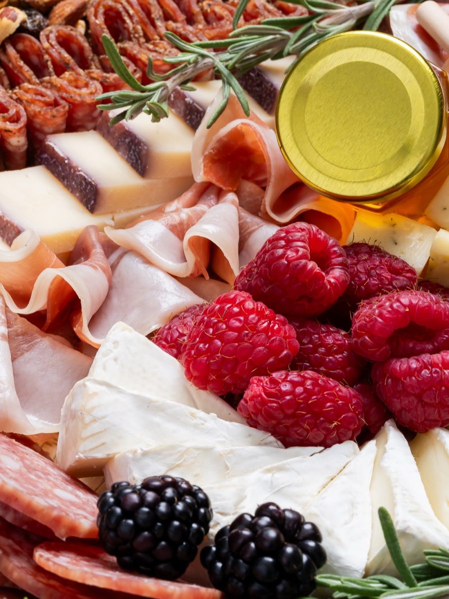 Una tabla de embutidos con quesos, carnes curadas y frambuesas
