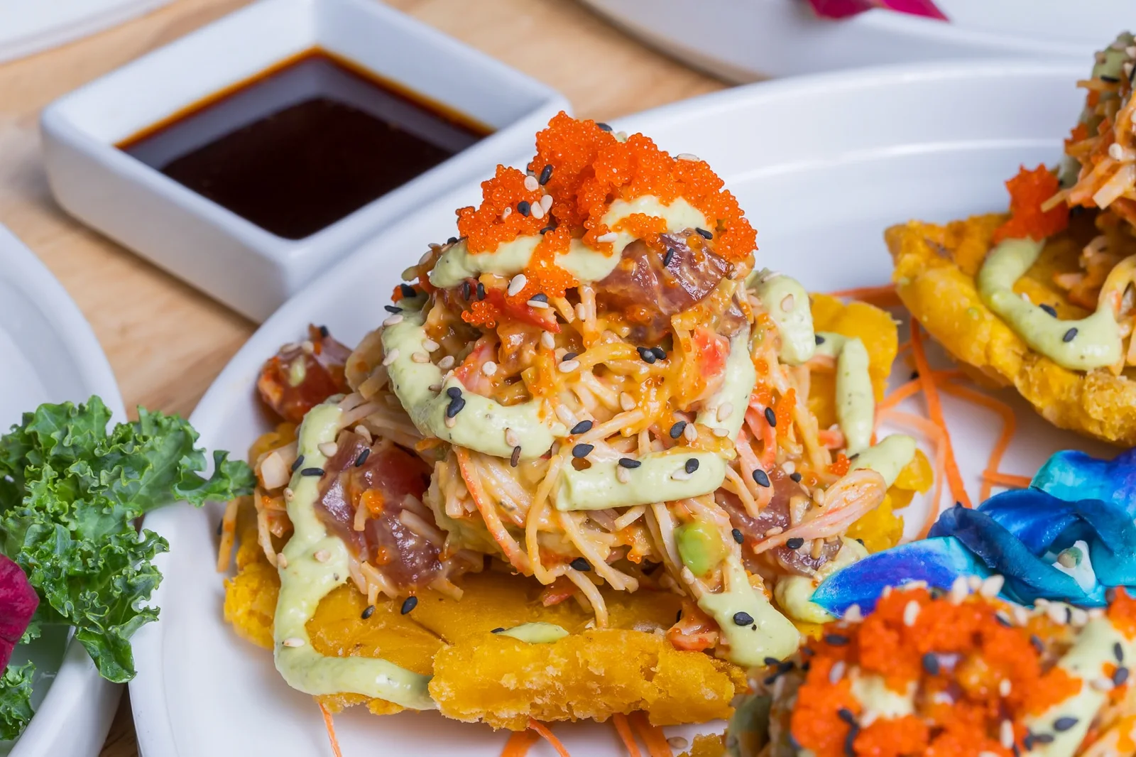 Tuna and crab with avocado crema and tobiko stacked on crispy tostones, soy dipping sauce beside