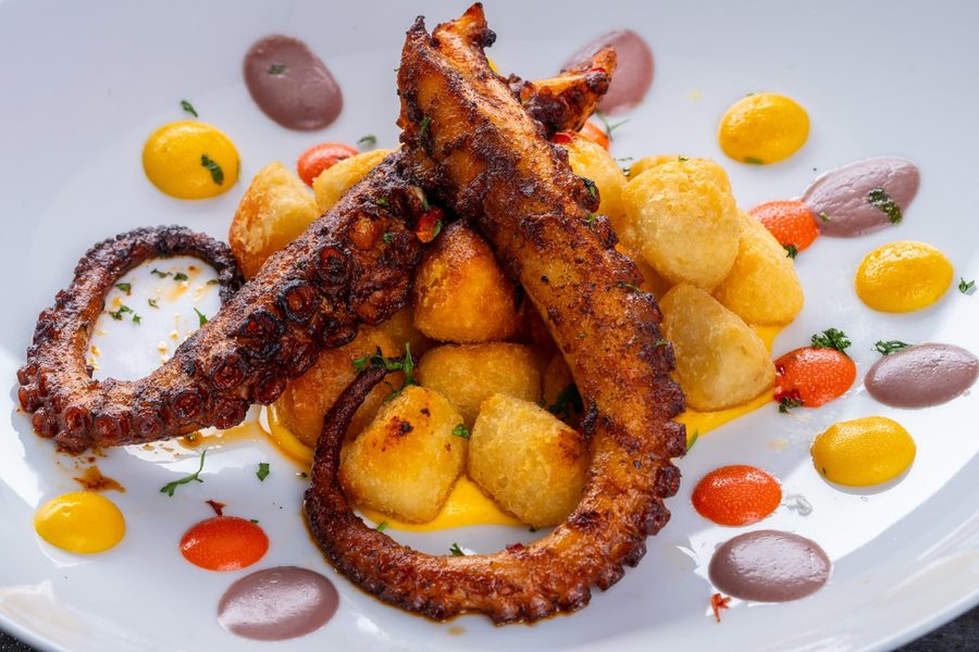 Charred octopus over crisp potatoes with dots of pepper sauce