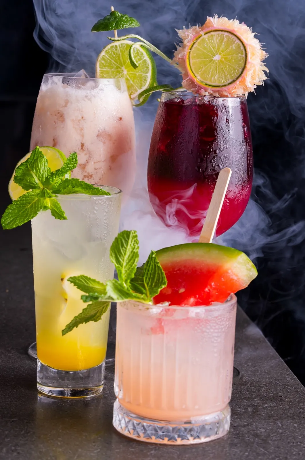 Three cocktails garnished with lime, mint and watermelon
