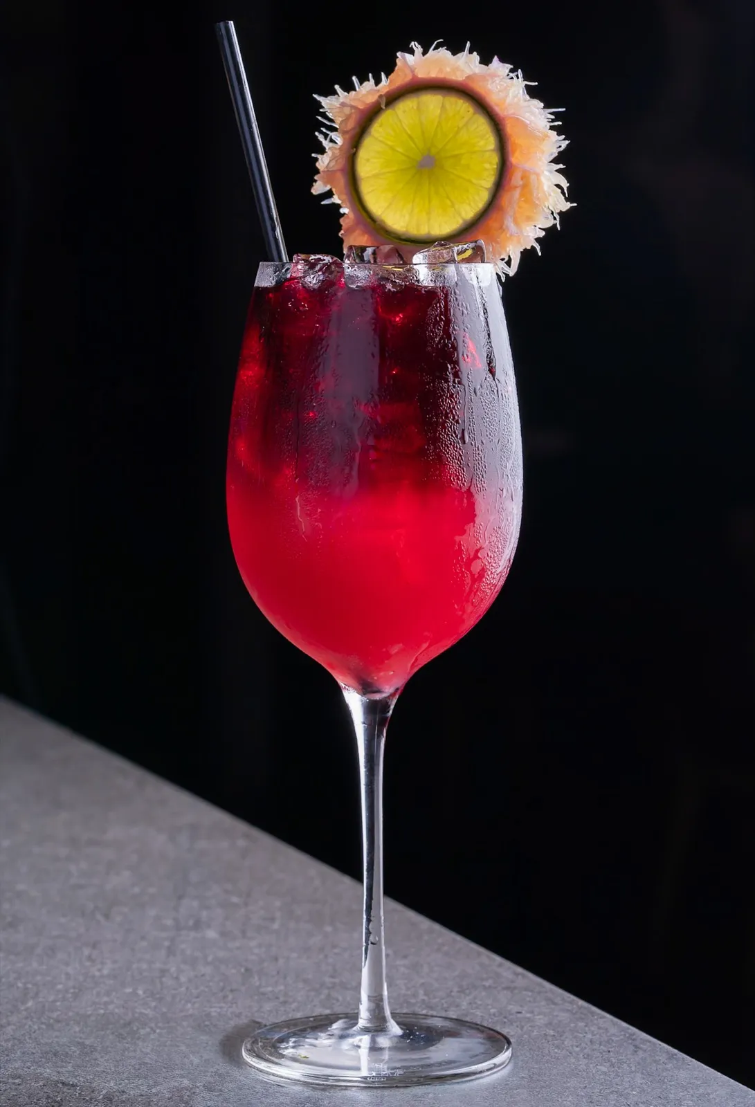 Un cóctel rojo con adorno cítrico, fotografiado sobre fondo negro para un menú de bebidas