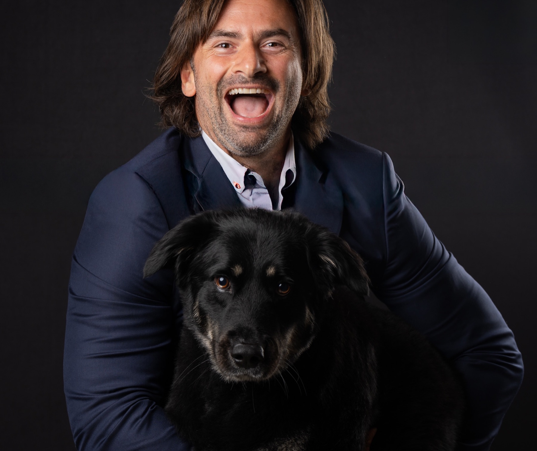 A man laughing while holding his dog for a studio portrait