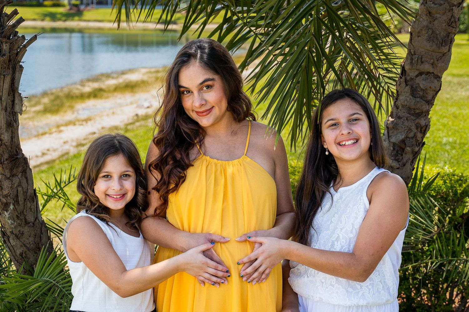 Expecting mother with her two young daughters under palm trees by the water