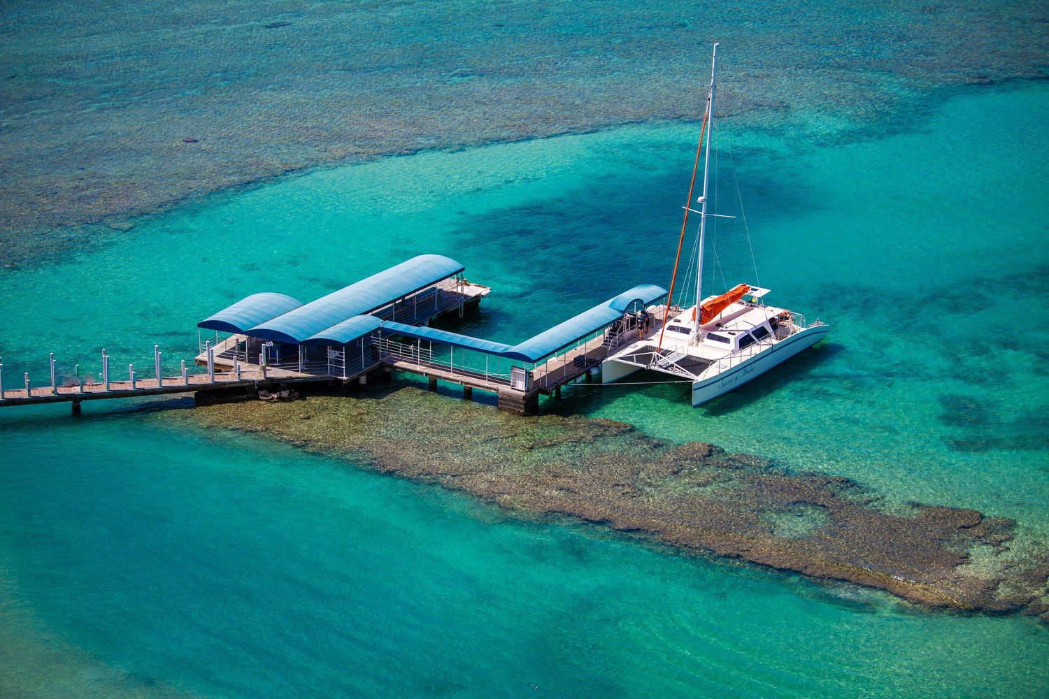 Aerial view of a dock and catamaran in turquoise water