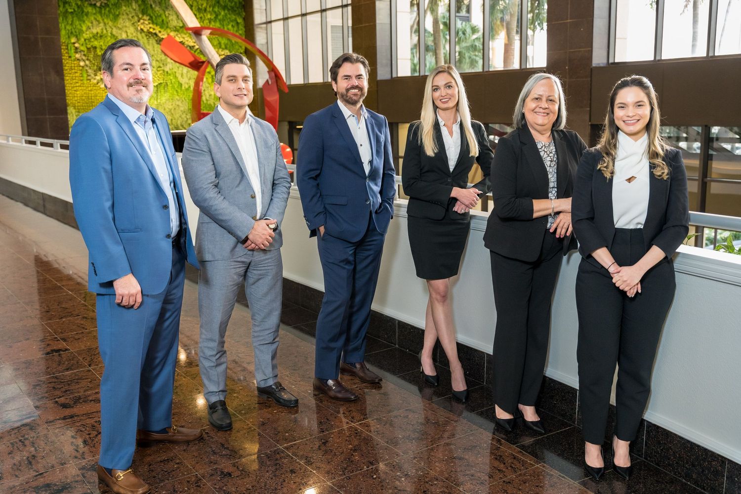 Six-person office team portrait beside a building's living plant wall