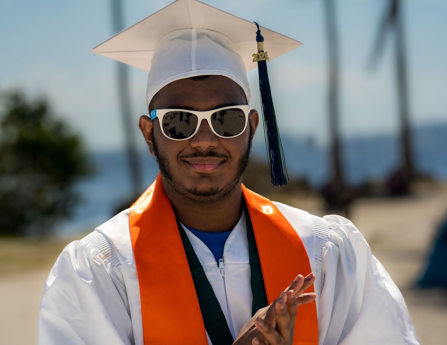 Close-up portrait of a smiling graduate in a cap, gown, and orange cord