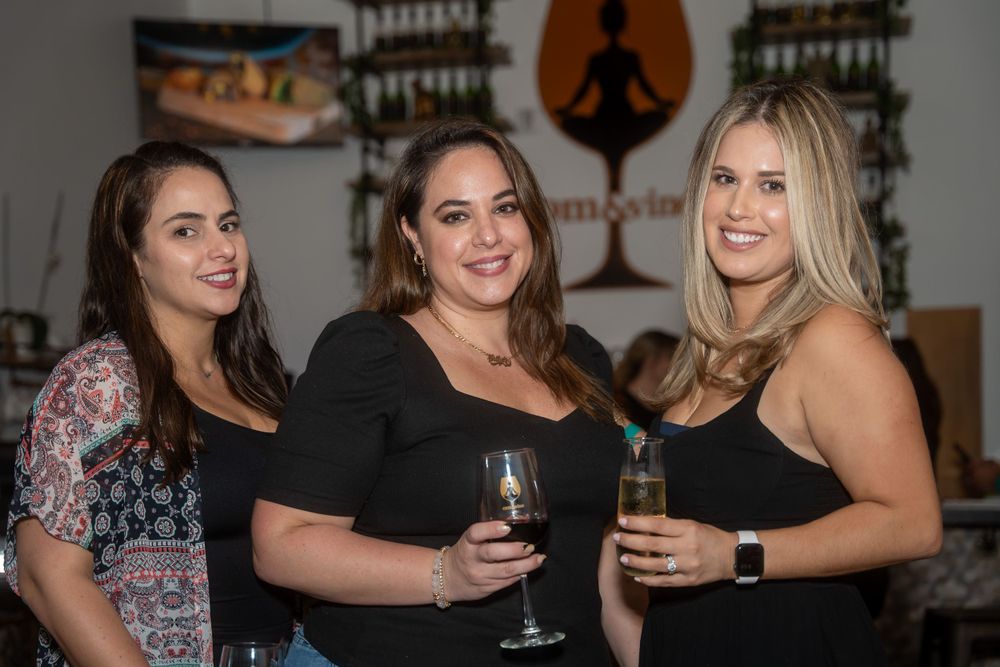 Three women smiling together holding wine glasses at a wine tasting event