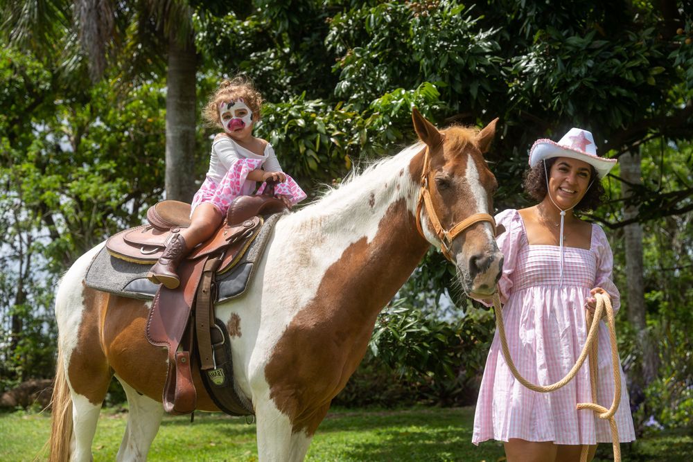 Young girl riding a horse led by a woman in a cowboy hat at an outdoor family event
