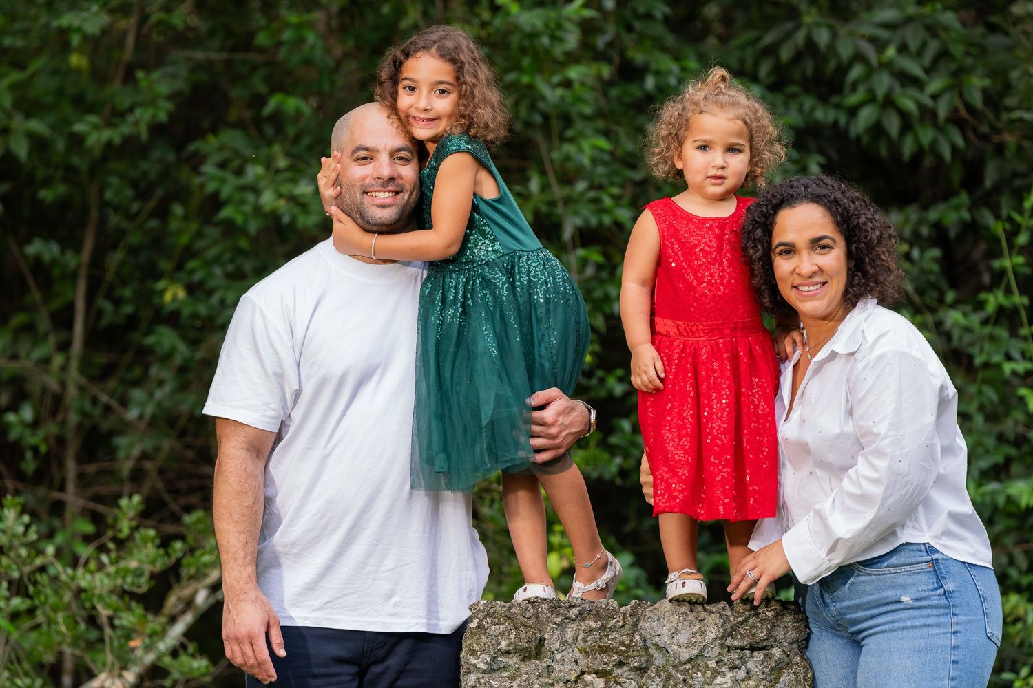 Family portrait with one daughter in a green sequin dress on her father's shoulders and another in red beside her mother