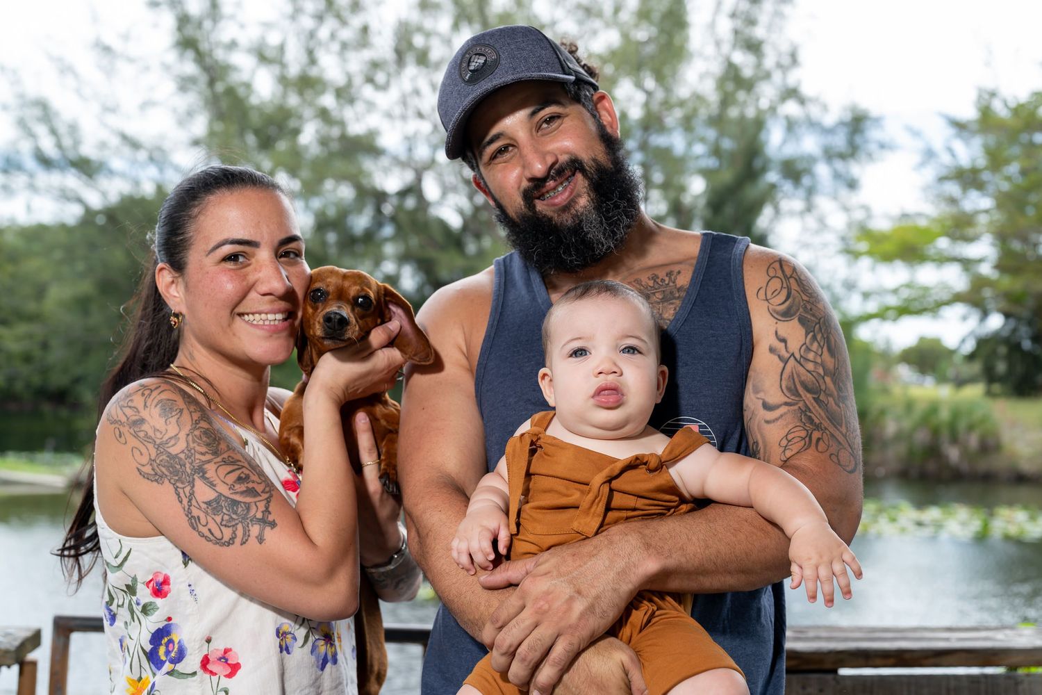 Parents holding their baby and their dachshund on a lakeside dock