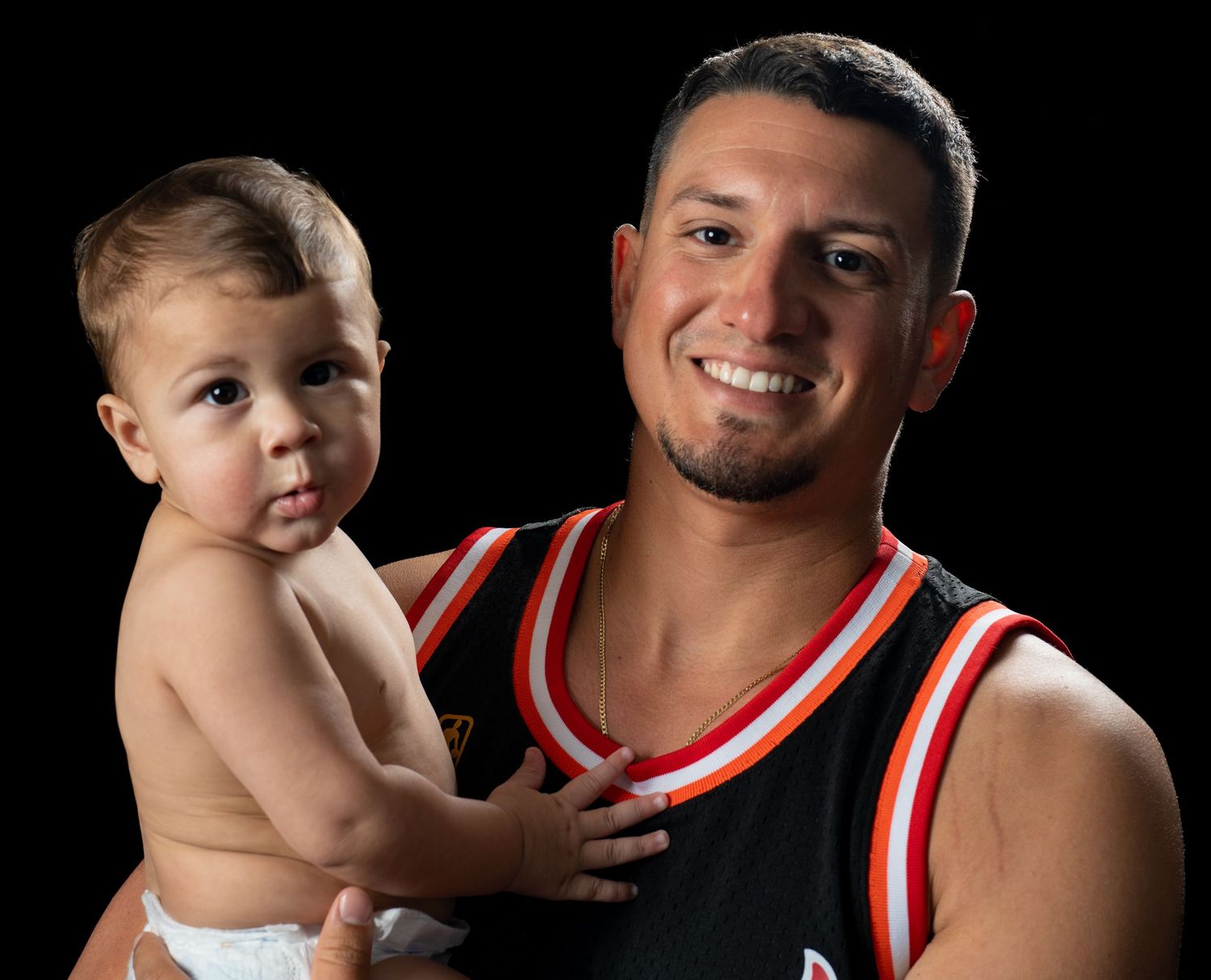 Father in a basketball jersey holding his baby son for a studio portrait