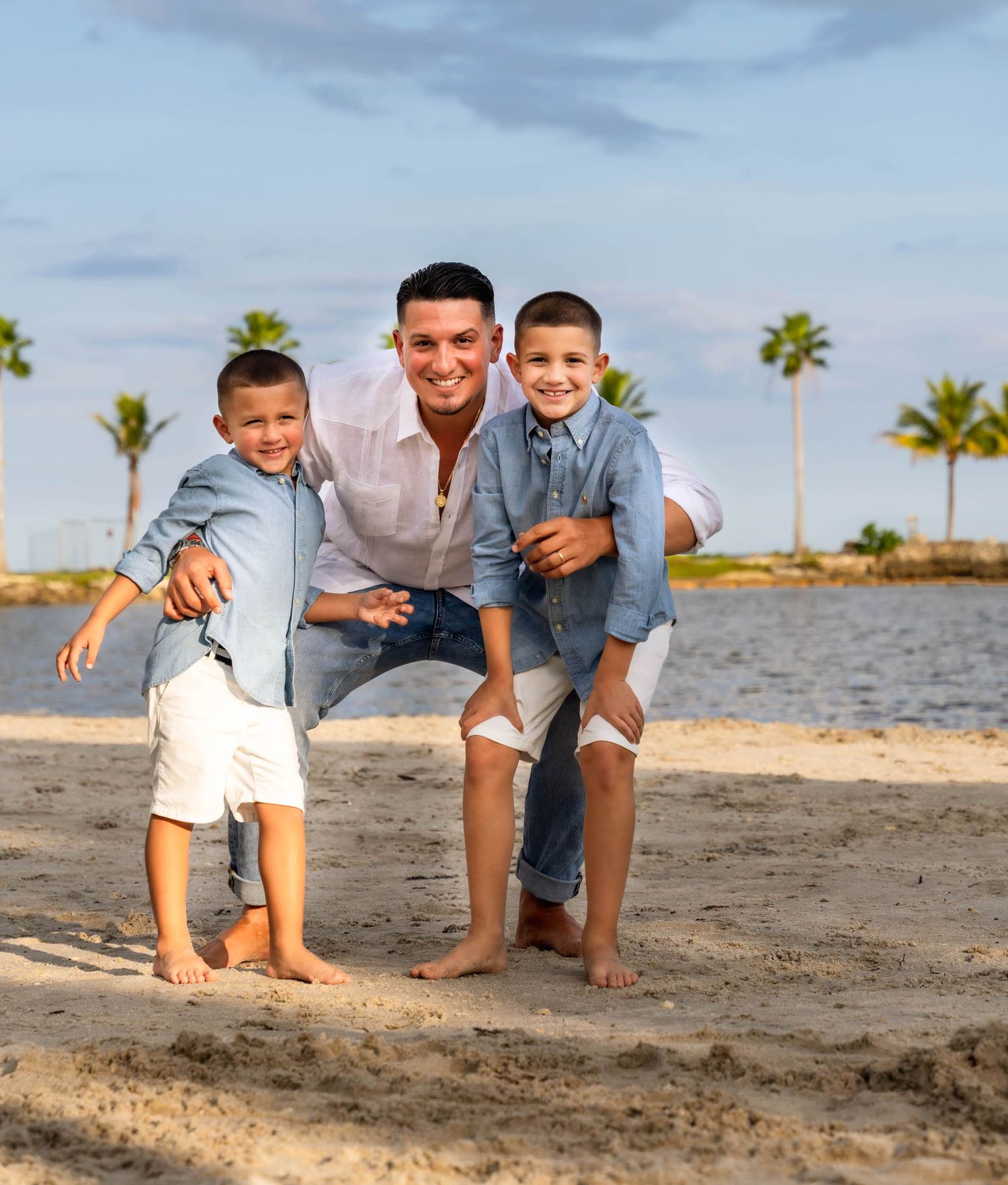 Father crouched between his two young sons in matching denim shirts on the beach