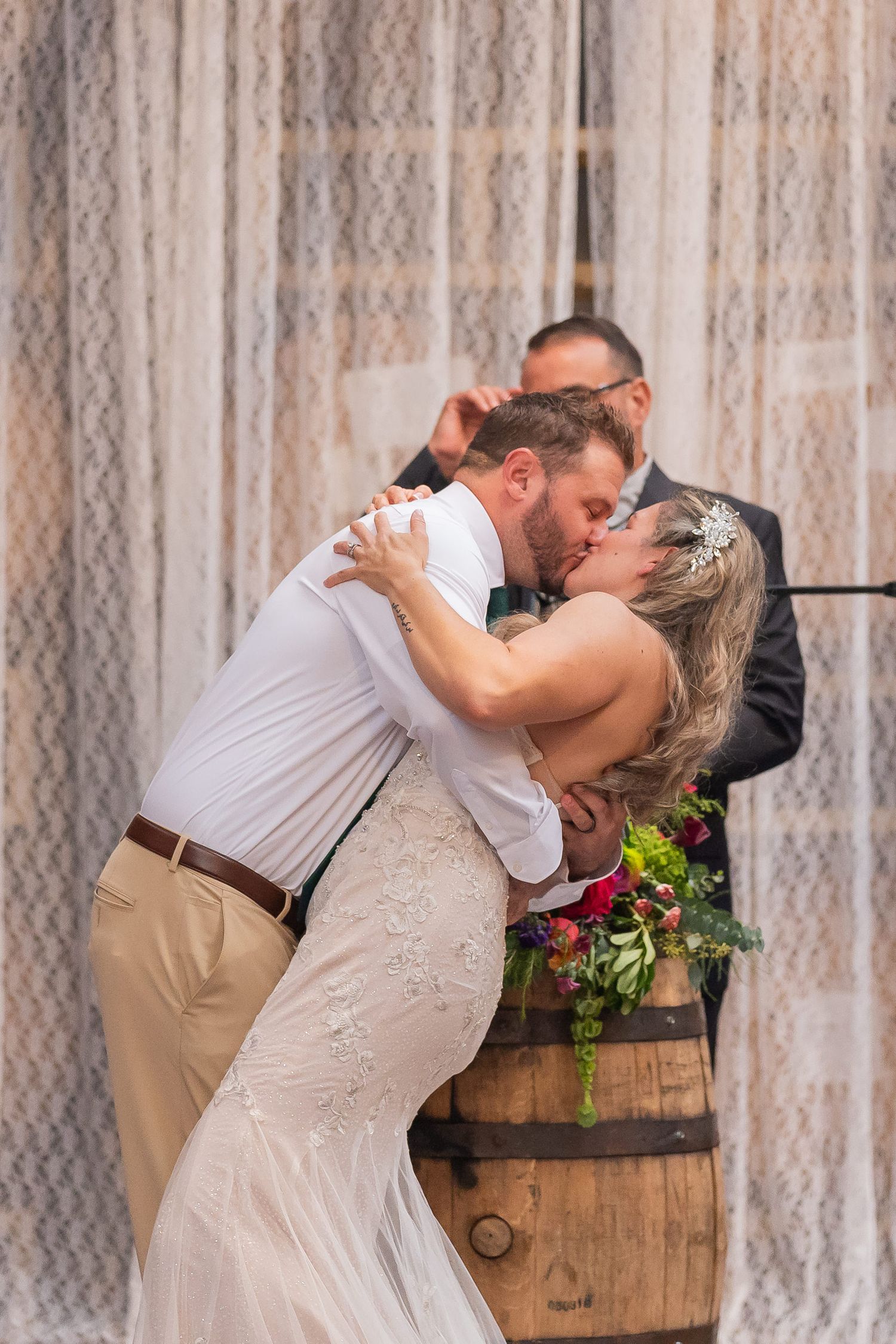 Groom dipping his bride for a kiss just after the ceremony, brewery barrels in the background