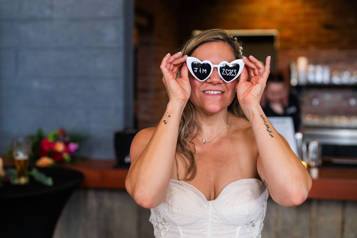 Bride wearing heart-shaped sunglasses reading the couple's initials and wedding year at the reception