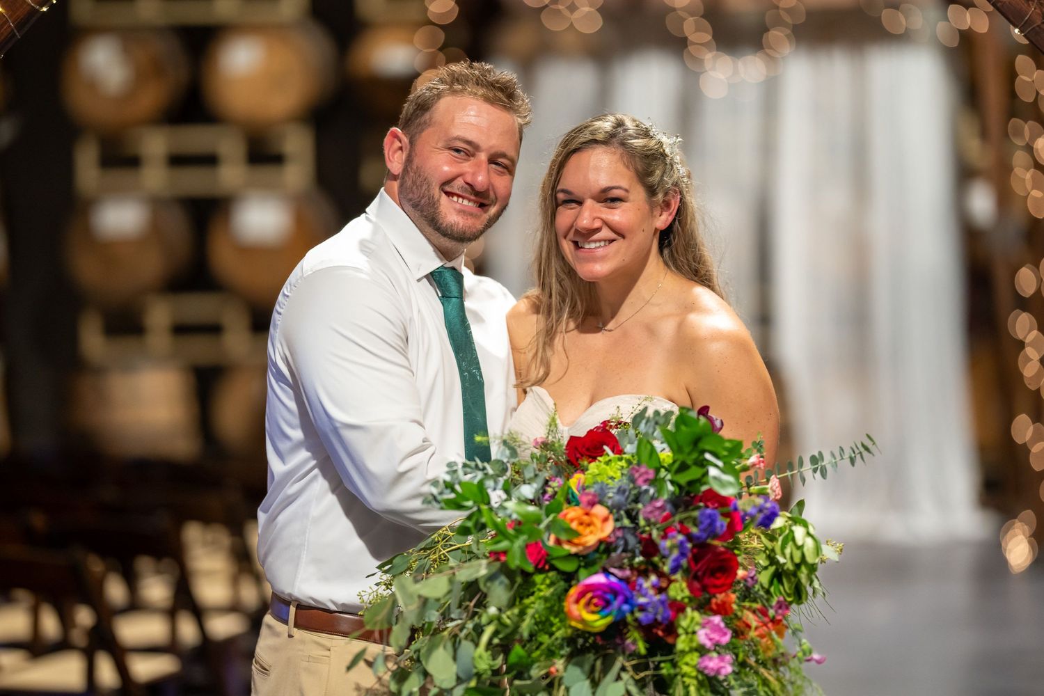 El novio y la novia sonríen con un ramo colorido en un salón de barriles