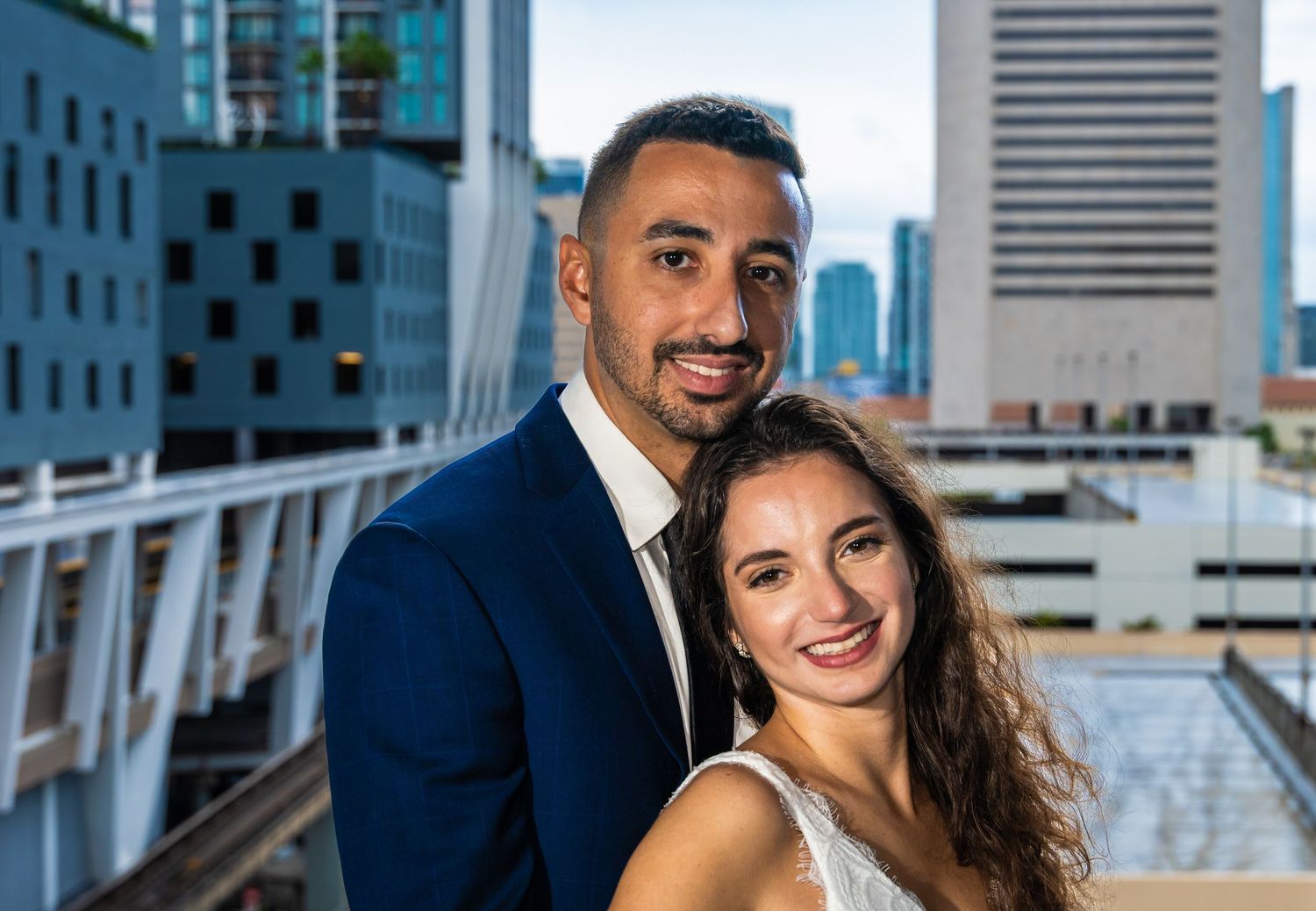 El novio con traje azul marino junto a la novia sonriente, con el horizonte de la ciudad detrás