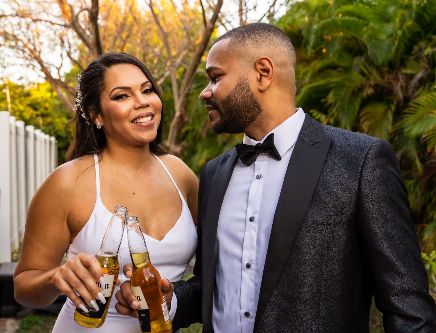 Los novios brindan con botellas de cerveza, sonriéndose entre hojas de palma