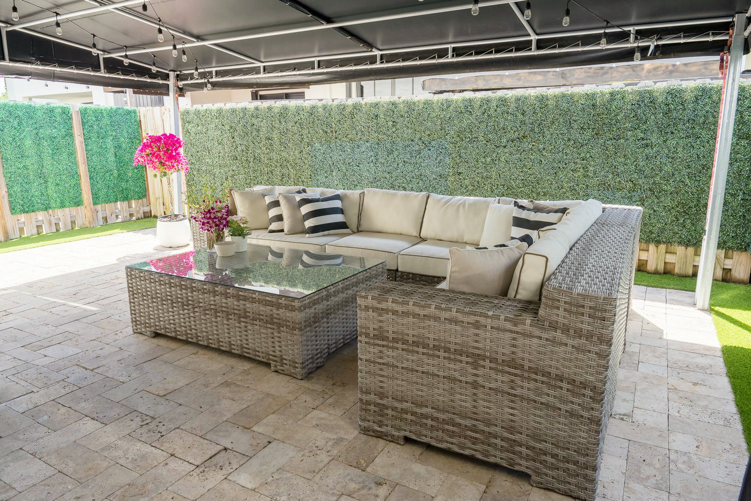 Terraza techada con un seccional de mimbre y guirnaldas de luces frente a un seto verde