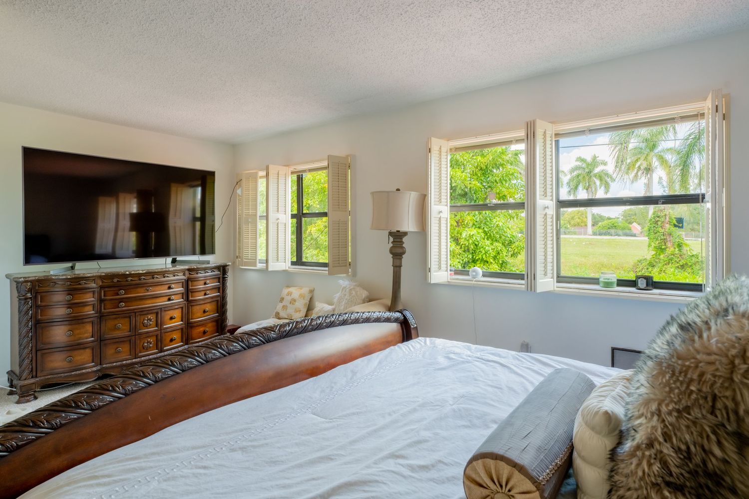 Bedroom with plantation shutters, a wall-mounted television, and natural light