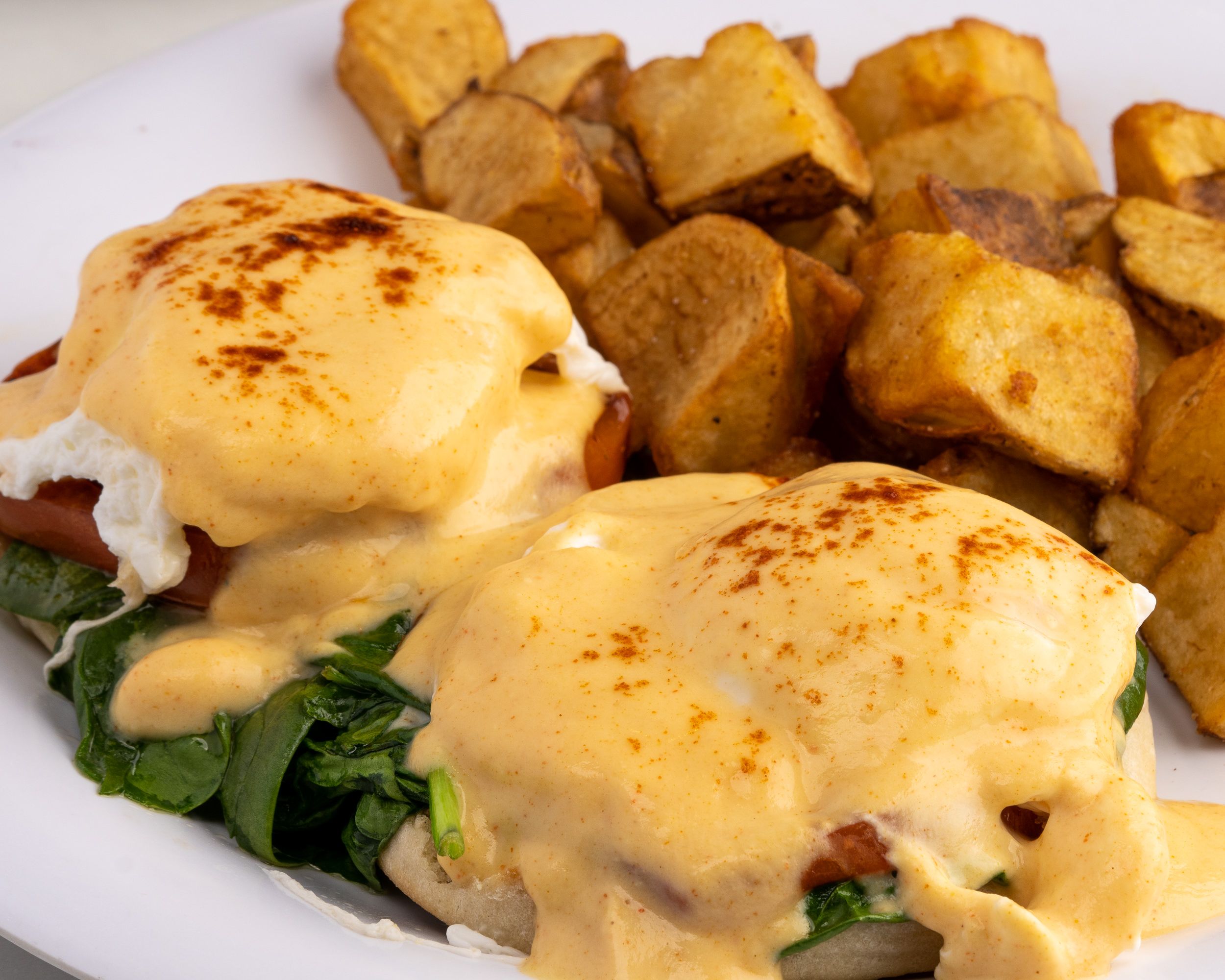 Eggs benedict plated with home fries