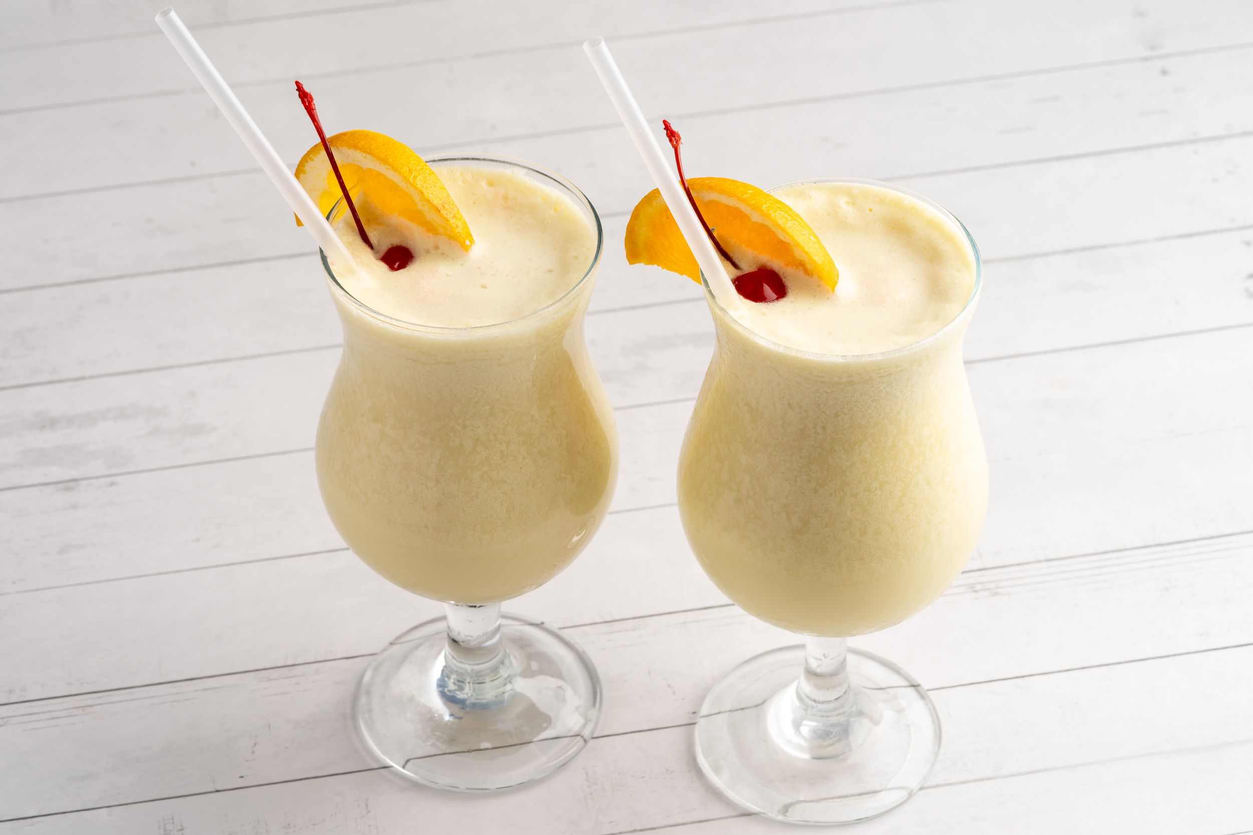 Two pina colada cocktails garnished with pineapple and cherry