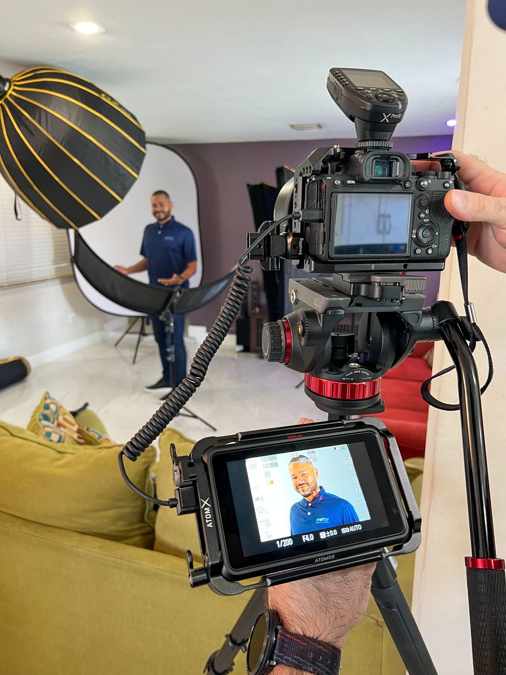 External monitor rig filming a man in a navy polo shirt in a softly lit living room