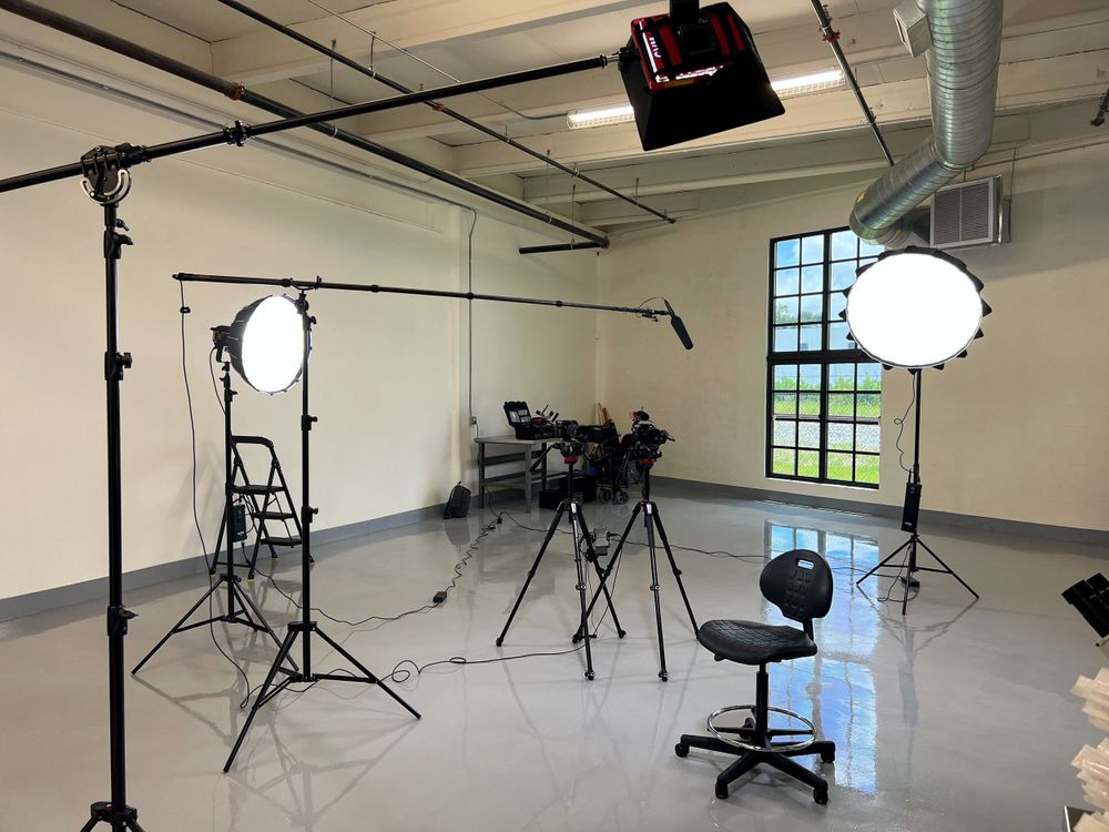 Un set de estudio vacío con luces en brazo, bases y un banco, iluminado y listo para una entrevista