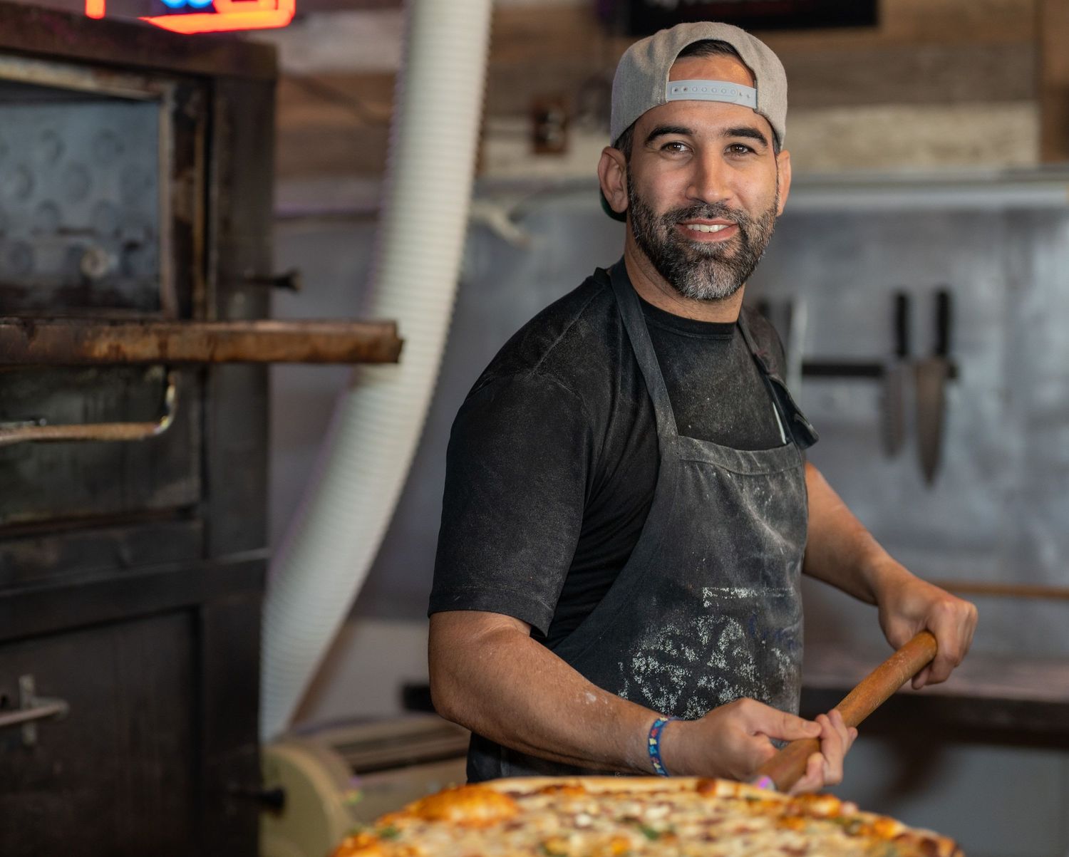 Retrato en locación de un chef sosteniendo una pizza recién hecha frente al horno