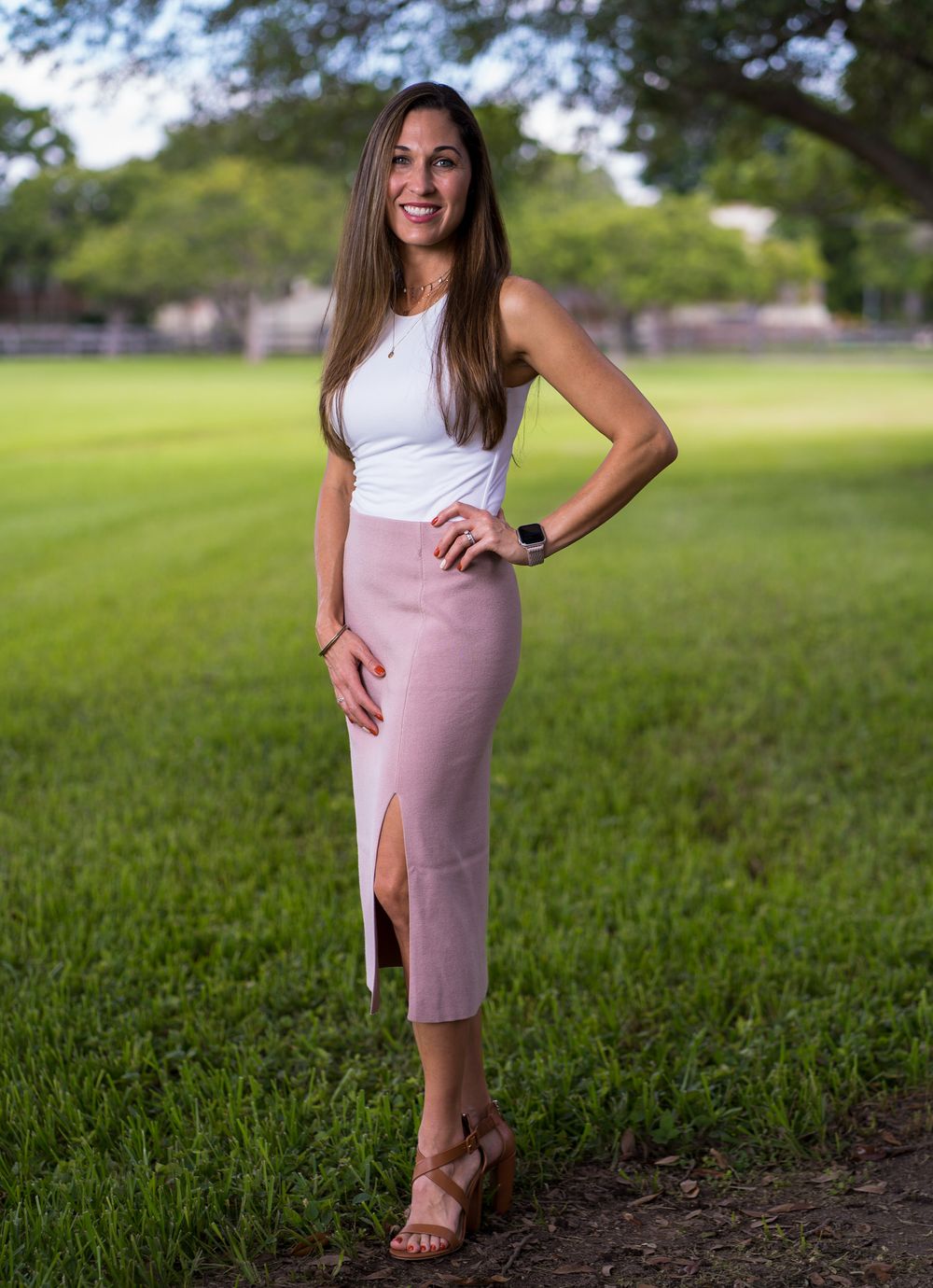 Woman in a white top and pink skirt standing on a park lawn with her hand on her hip