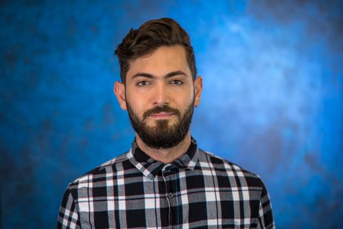 Studio headshot of a bearded man in a plaid shirt against a blue backdrop