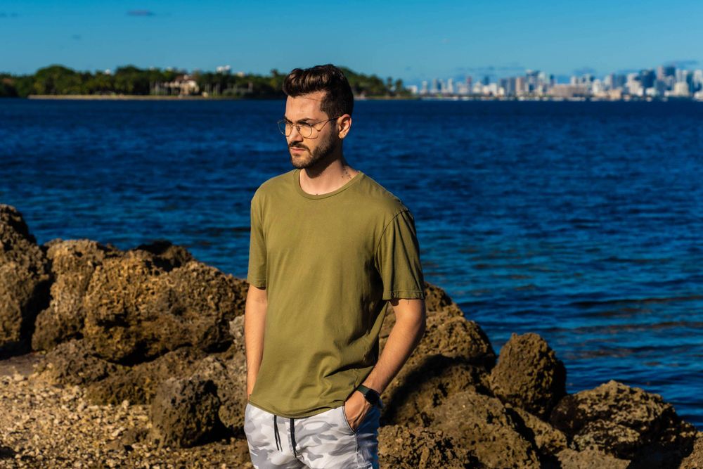 Male model standing on the rocks with the Miami skyline and water behind him