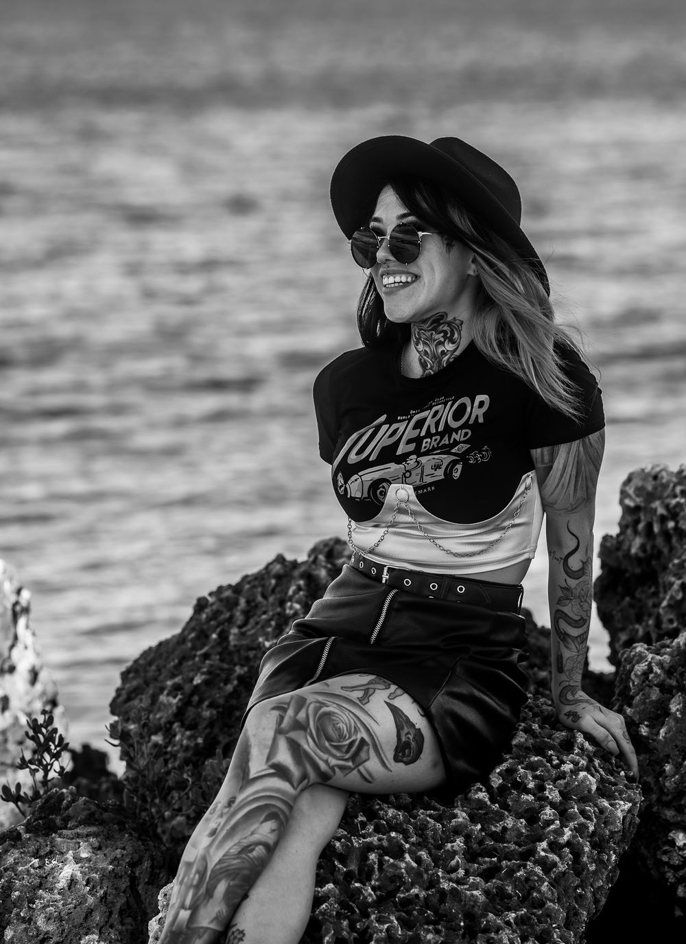Black and white portrait of a model sitting on the rocks by the water, smiling